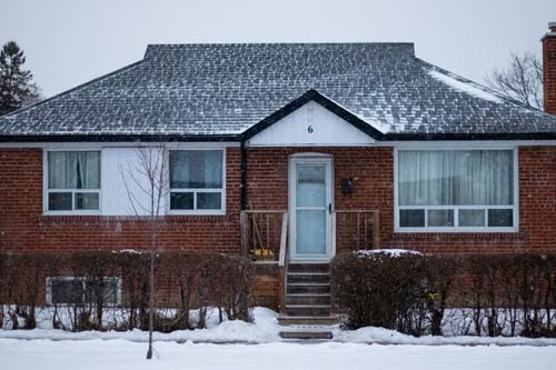 A brick bungalow in winter with snow on the roof
